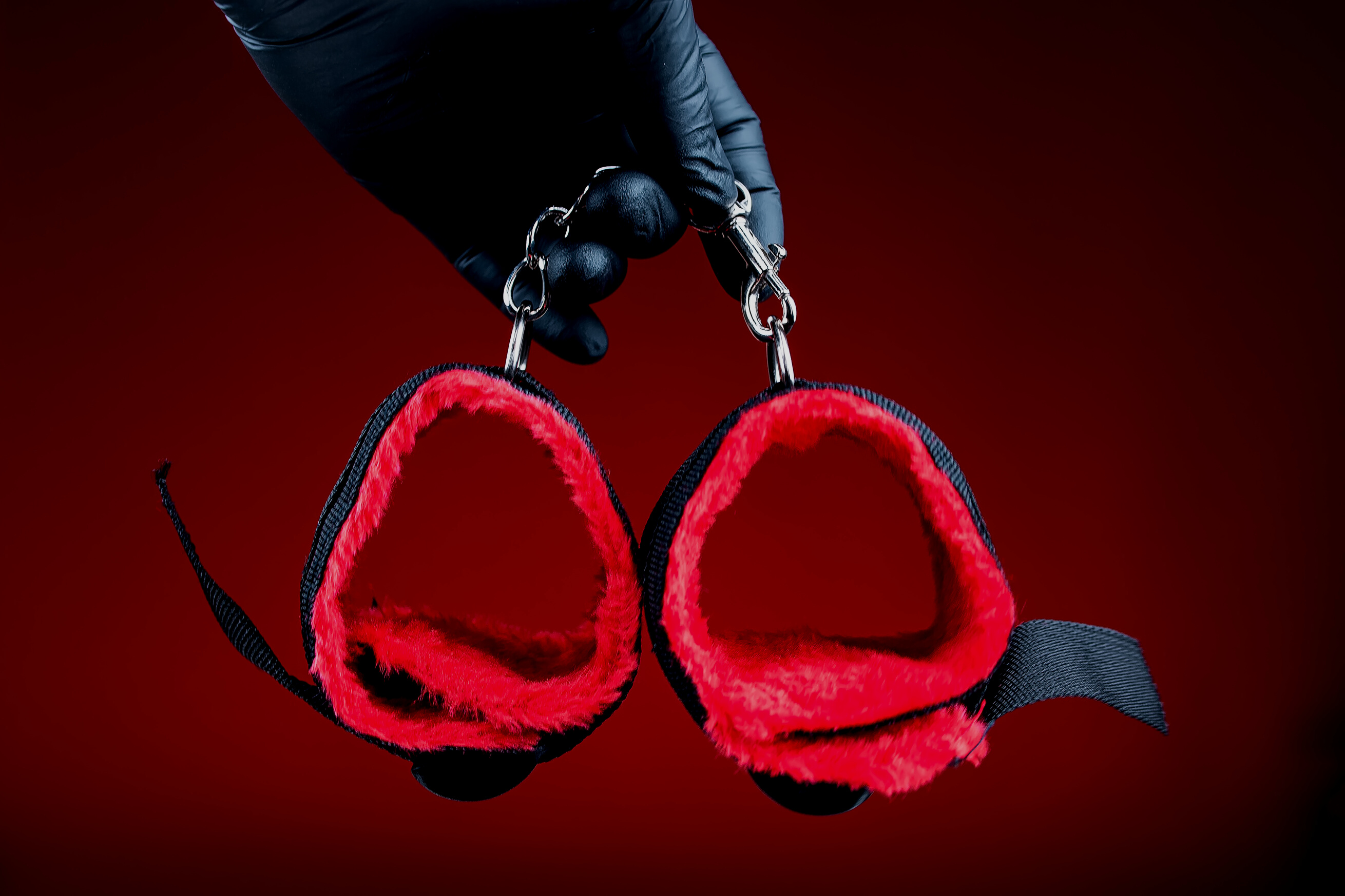 Hands in Black Gloves Holding Handcuffs with Red Belts for